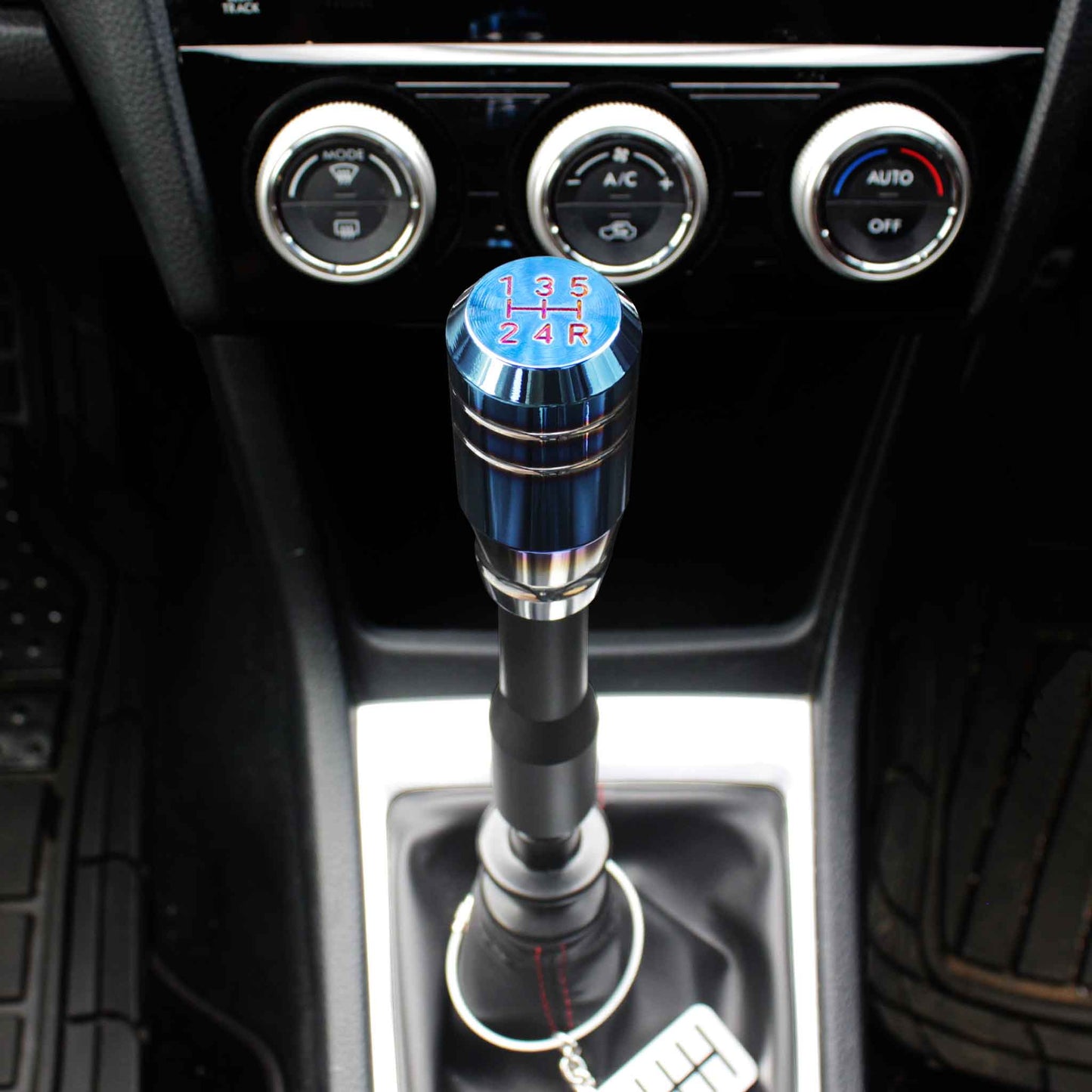 A burnt blue shift knob is installed on a manual WRX with an extension between the knob and the shift boot, and a six-speed dog-tag is hanging around the shift boot