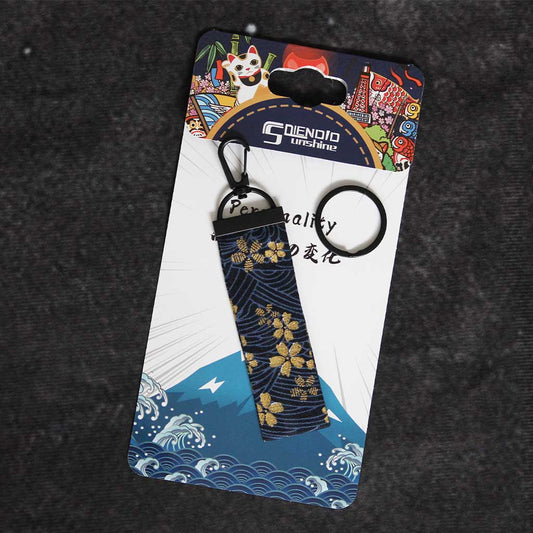 A cherry blossom wafu keychain placed on a Japanese style packaging on a grey background