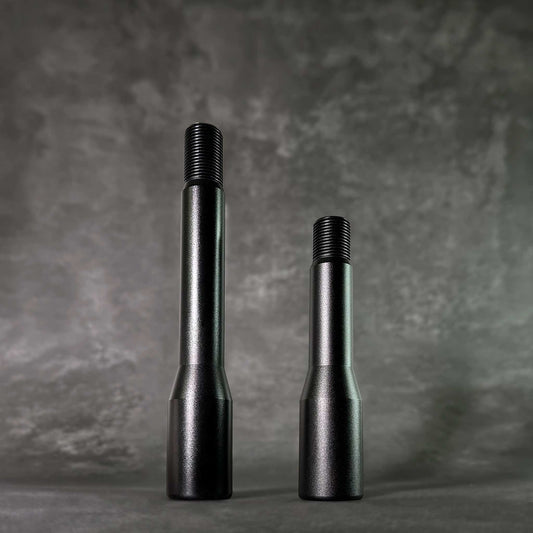 Two black shift knob extensions in different height standing on a grey floor on a grey background