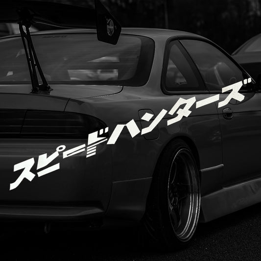 A white Speed Hunters in Japanese car vinyl decal placed pointing to the screen with a darkened vintage car at the back