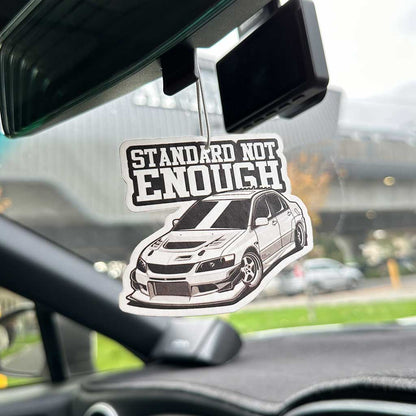 A Mitsubishi Evolution with the writing 'standard not enough' hung on a car's rearview mirror