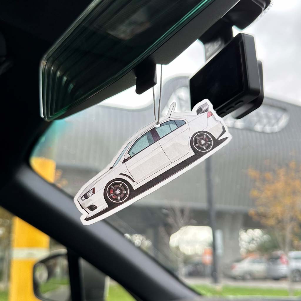 A Mitsubishi EVO air freshener hung on a car's rearview mirror with the background blurred