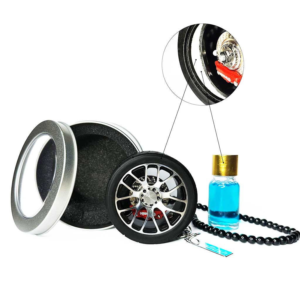 A black BBS wheel air-freshener standing on a white floor with a metal box as well as a bottle of fragrance behind it, and also a bubble around it showcasing its details