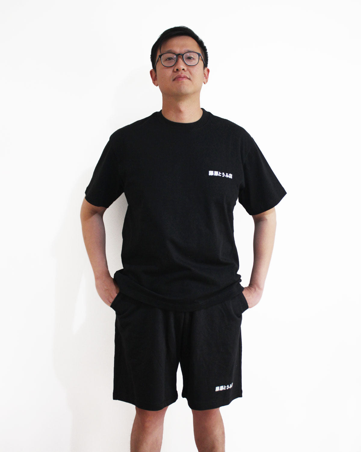 An asian wearing a set of Initial-D-themed clothing, including short-sleeved T-shirt and short pants standing in front of a white wall