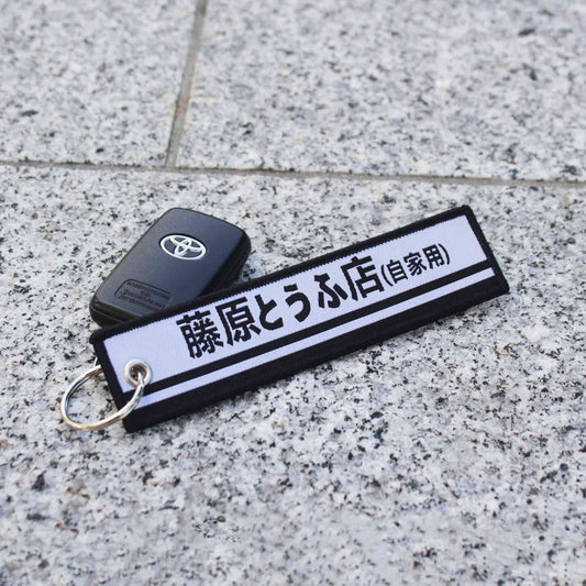 A black and white jet tag with the writing 'Fujiwara Tofu Shop' holding a Toyota car key on a marble floor