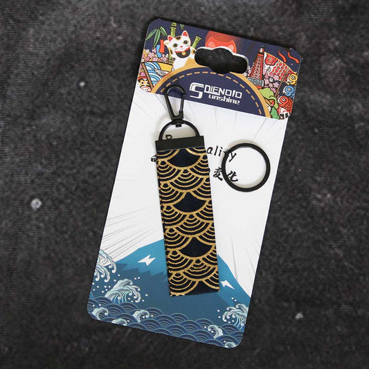 A gold wave wafu keychain placed on a Japanese style packaging on a grey background