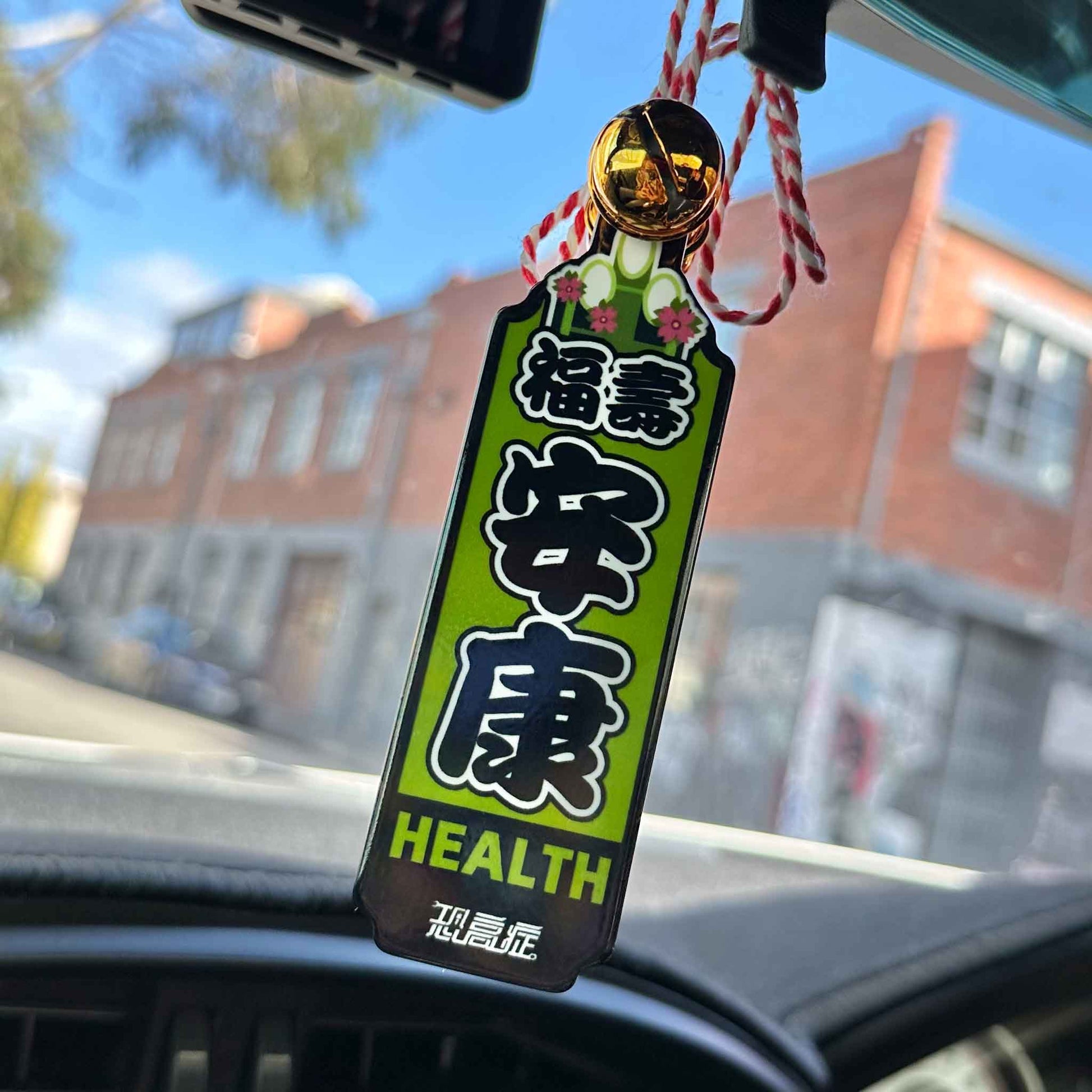 A green Japanese charm meaning 'healthy life' hung on a car's rearview mirror