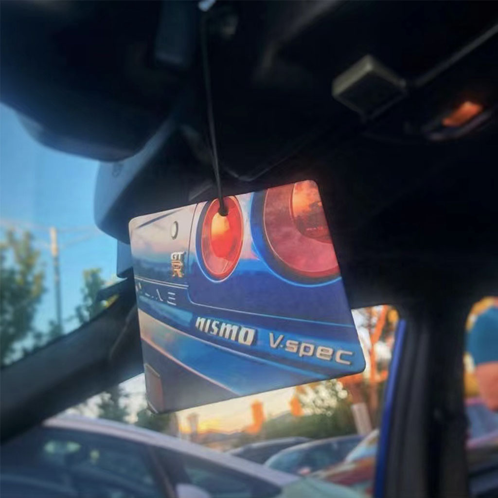 An air freshener with a pattern of the tail lights of a Skyline GTR R34 and some nismo related characters hung on a car's rearview mirror