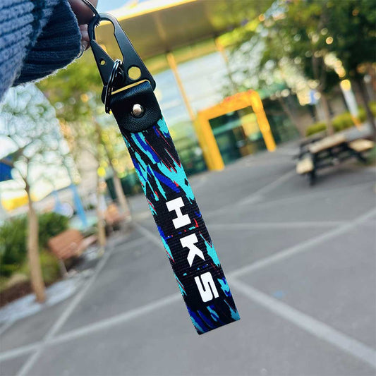 A HKS lanyard held by a hand in an open area