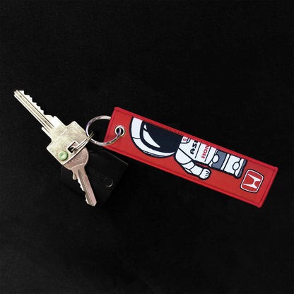 A Honda Asimo jet tag holding two door keys on a black background