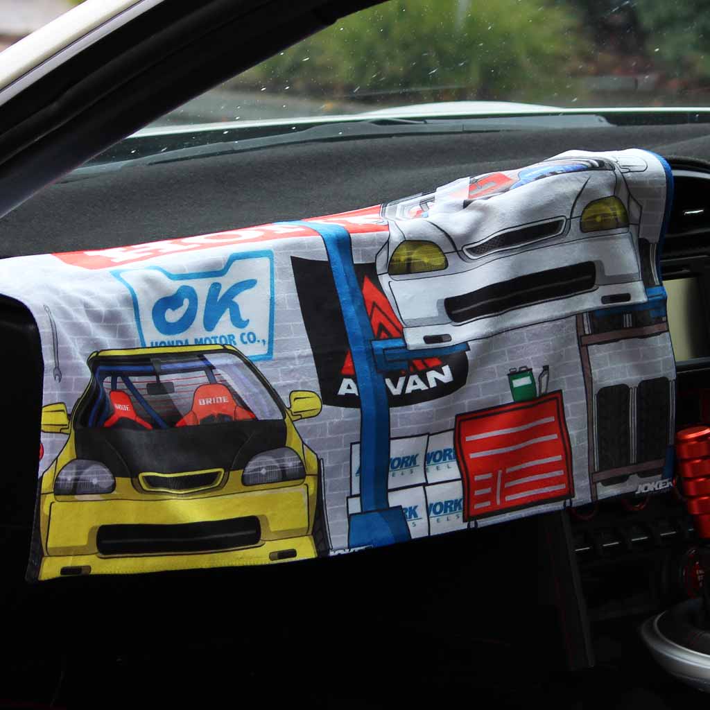 A car towel featuring two Honda cars at a work shop is placed on a car's centre console