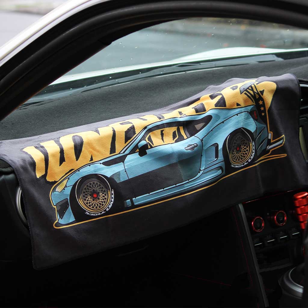 A car towel featuring a wide body BRZ and the yellow writing 'I love haters' is placed on a car's center console