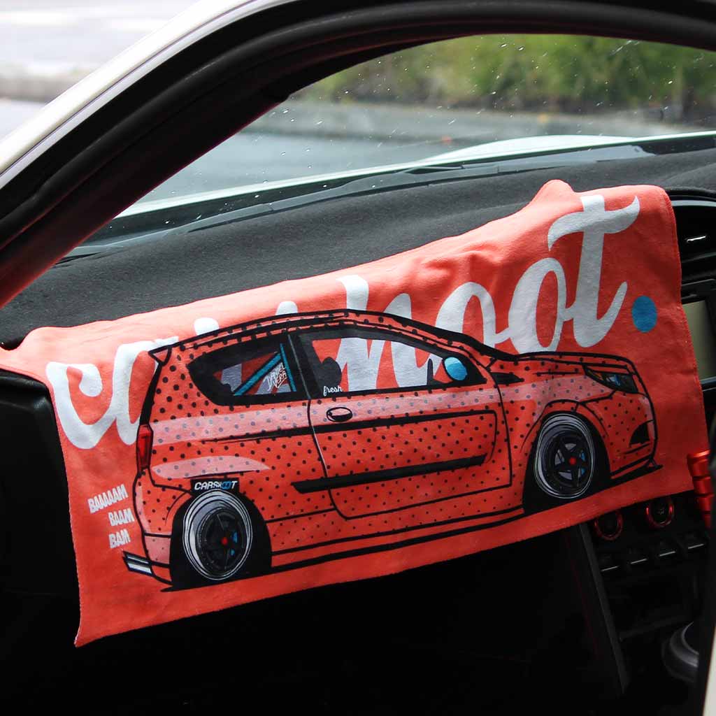A car towel featuring a wagon Japanese car and the white writing 'car shoot' is placed on a car's centre console