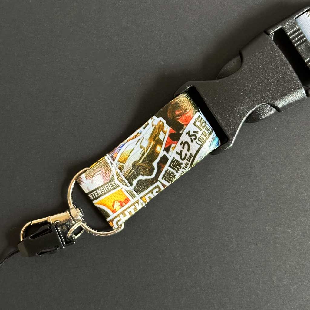 Close-up of the buckle of an Initial-D-themed keychain with Fujiwara Tofu Shop characters on a black background