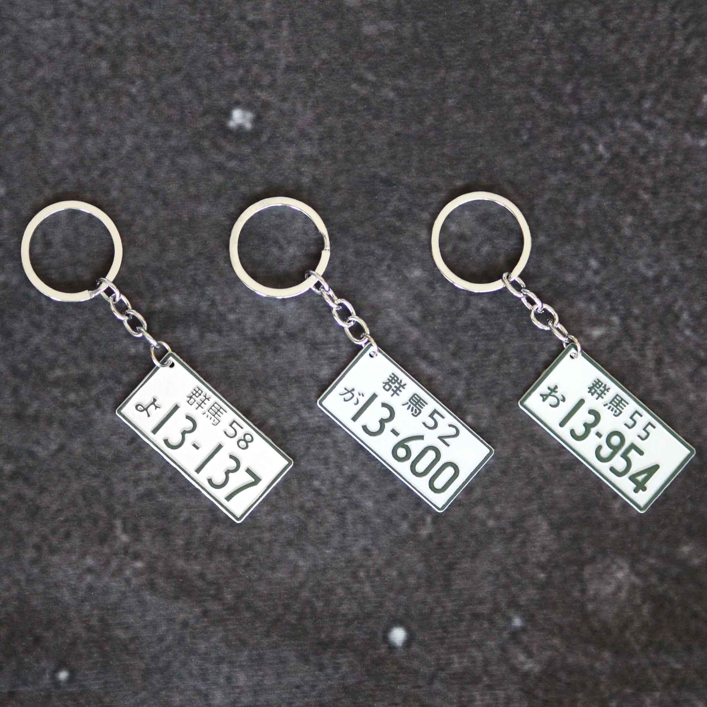 Three metal keychains featuring different number plates placed neatly on a grey background