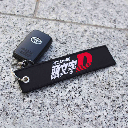 A black and white jet tag with the Japanese writing 'Initial-D' holding a Toyota car key on a marble floor