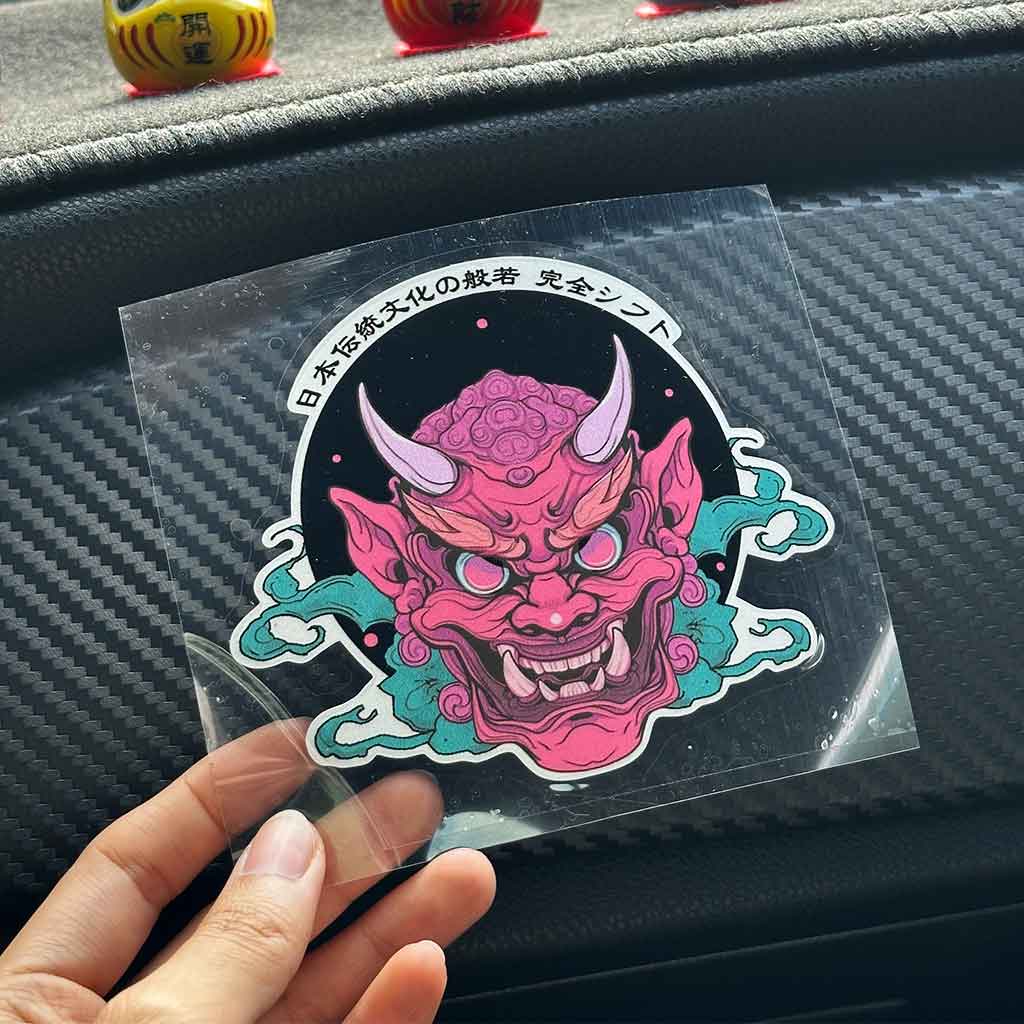 A hand holding an Oni mask style JDM sticker