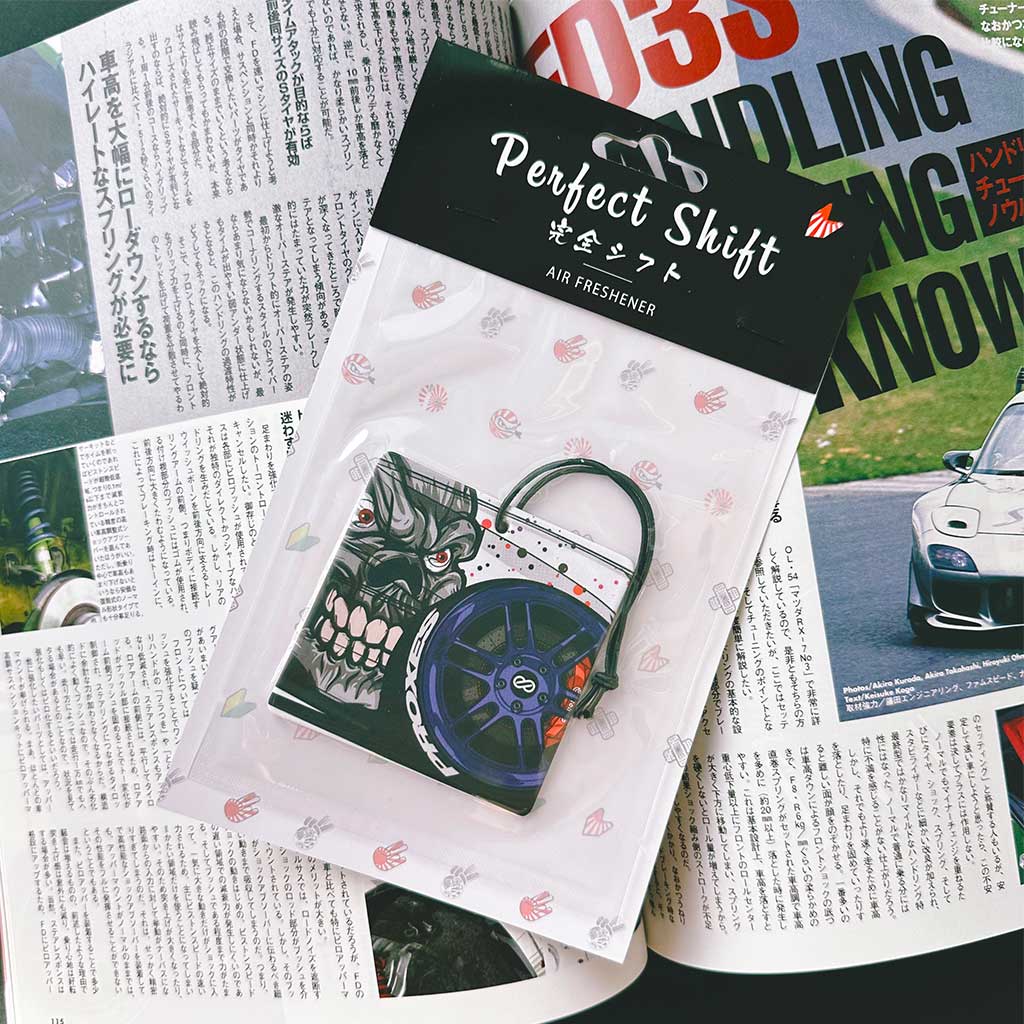 A JDM car air freshener themed evil and blue wheel flat laid on a Japanese magazine