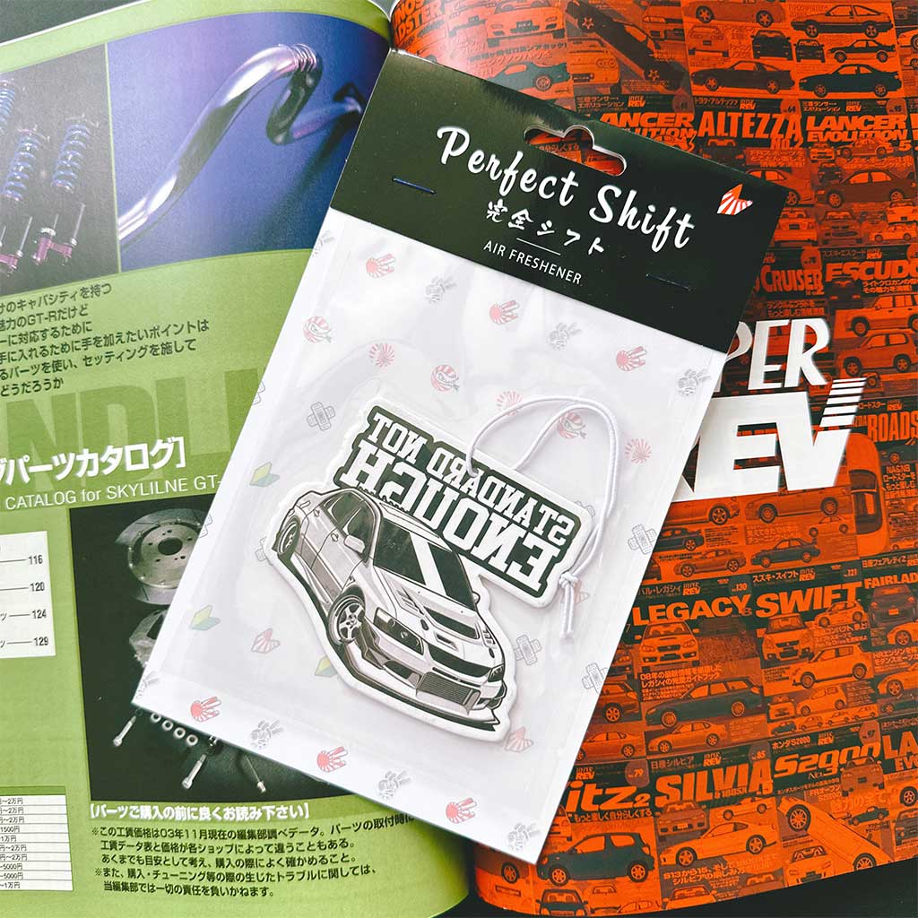 A JDM car air freshener themed Mitsubishi Evolution 8 flat laid on a Japanese magazine