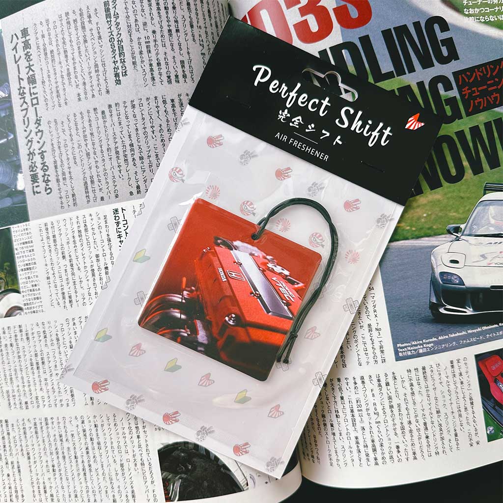 A JDM car air freshener themed Honda V-tec engine flat laid on a Japanese magazine
