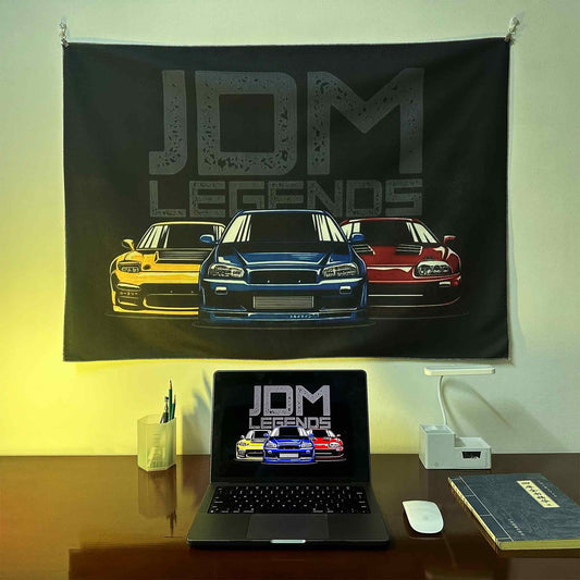 A JDM Legends artwork hung on a wall, with a laptop showing the same photo as the wall poster underneath, lit by yellow spotlight