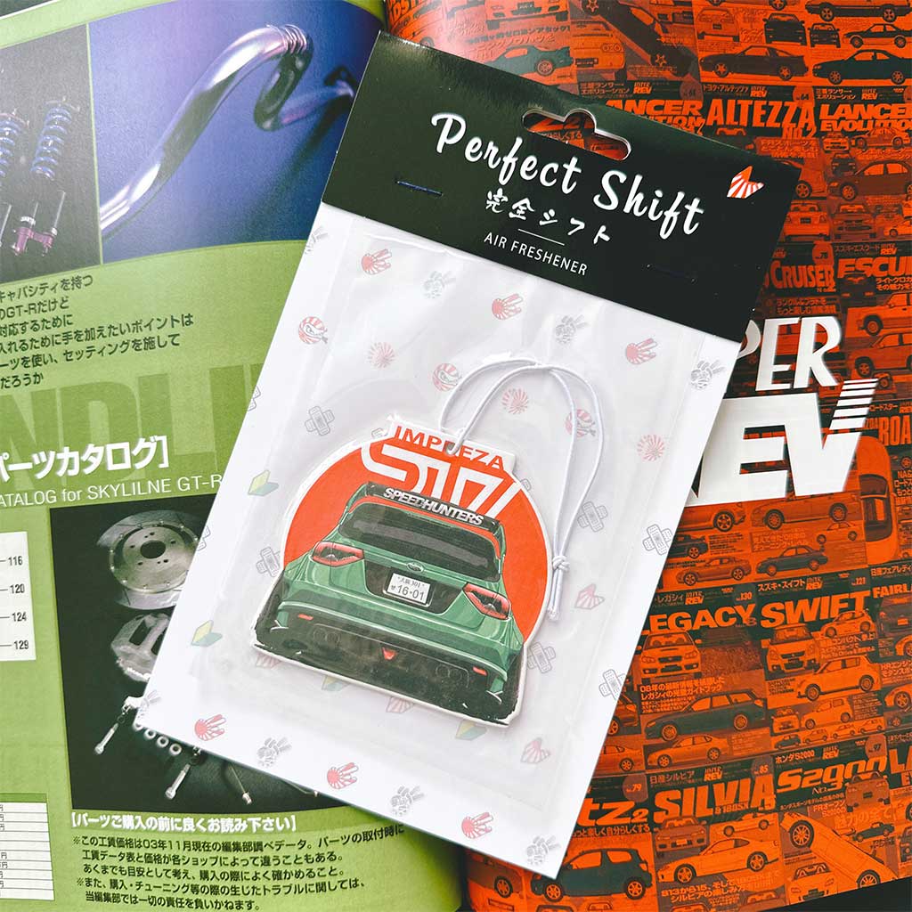 A JDM car air freshener themed Subaru STI flat laid on a Japanese magazine