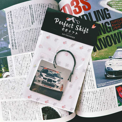 A JDM air freshener themed Subaru rally car flat laid on a Japanese magazine