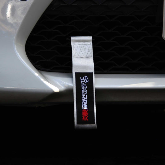A silver and black Osaka JDM tow strap installed on a white car's front grille