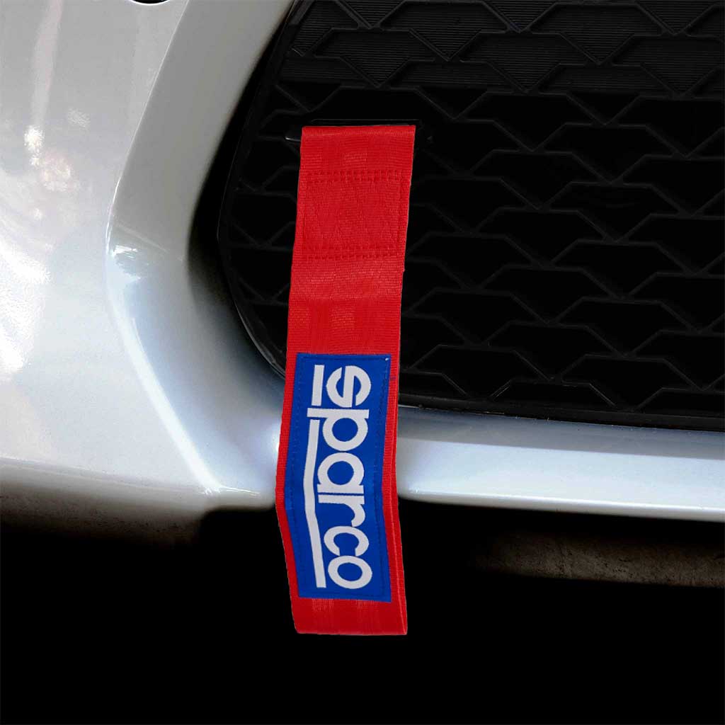 A red Sparco JDM tow strap installed on a white car's front mesh