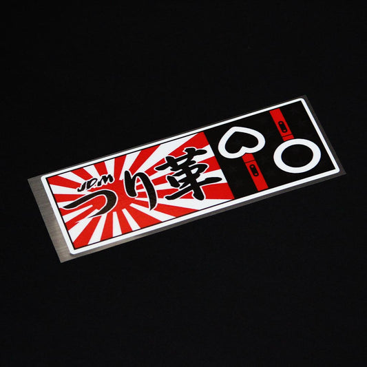 A red JDM Tsurikawa slap sticker flat laid on a black background