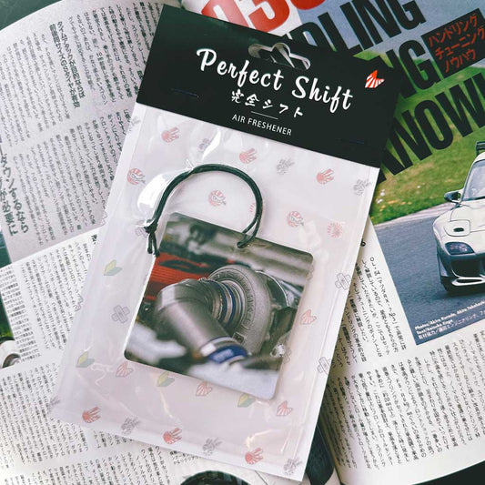 A JDM car air freshener themed HKS turbo flat laid on a Japanese magazine