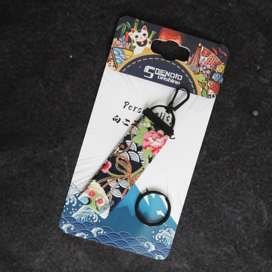 A Flying Crane wafu keychain placed on a Japanese style packaging on a grey background
