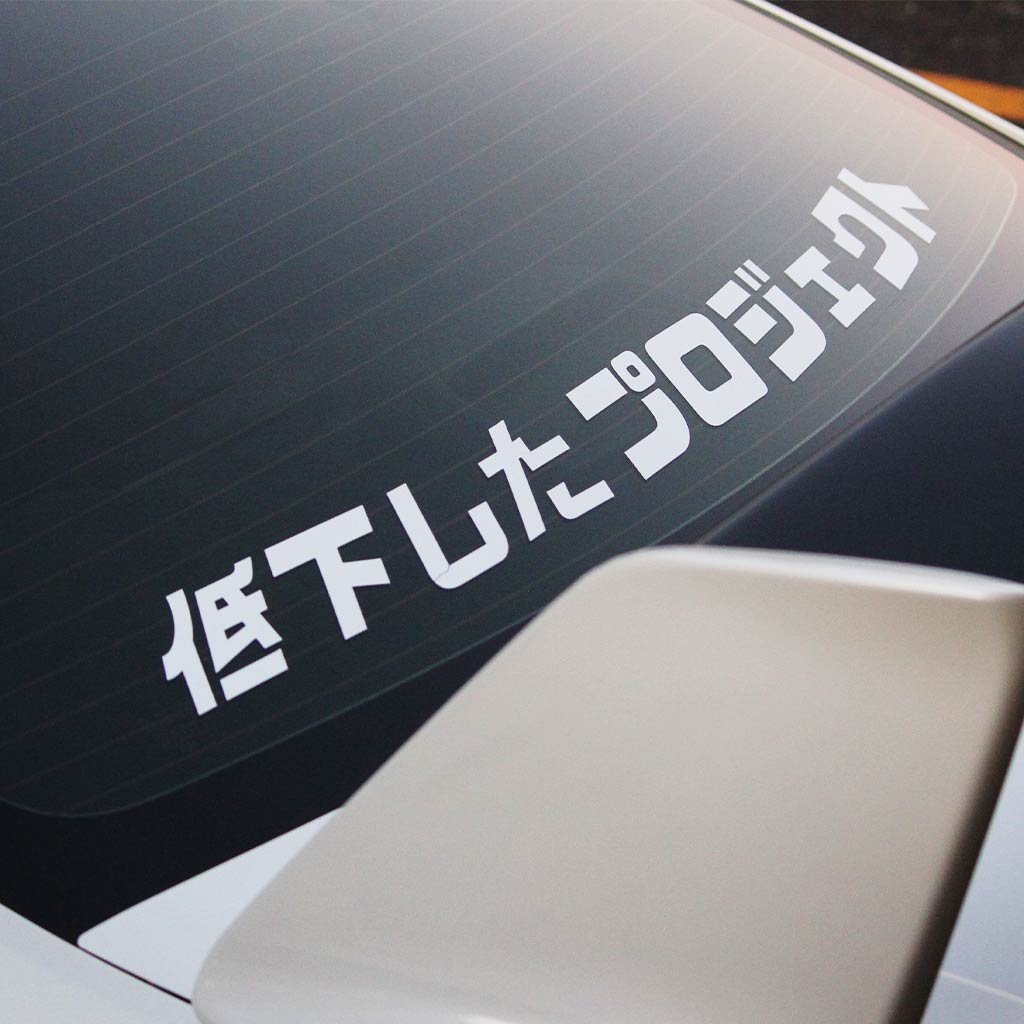 A white Lowered Project car vinyl decal applied on a white car's rear window, and the car has a big spoiler