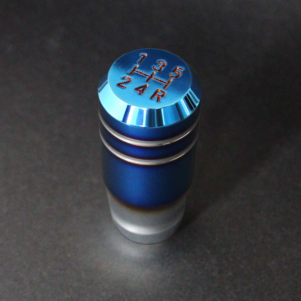 The burnt blue shift knob for manual cars is standing upright on a dark grey background