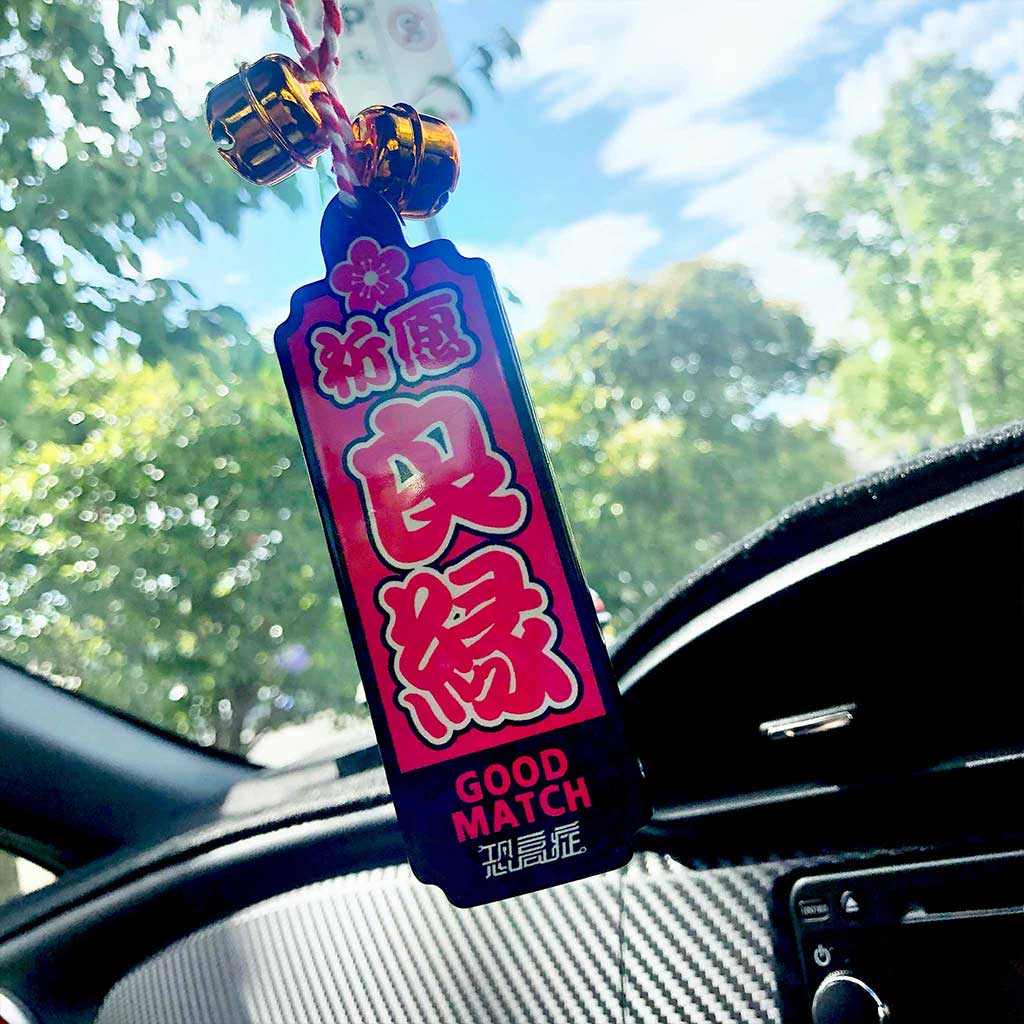 A pink Japanese charm meaning 'good luck in love' hung on a car's rearview mirror