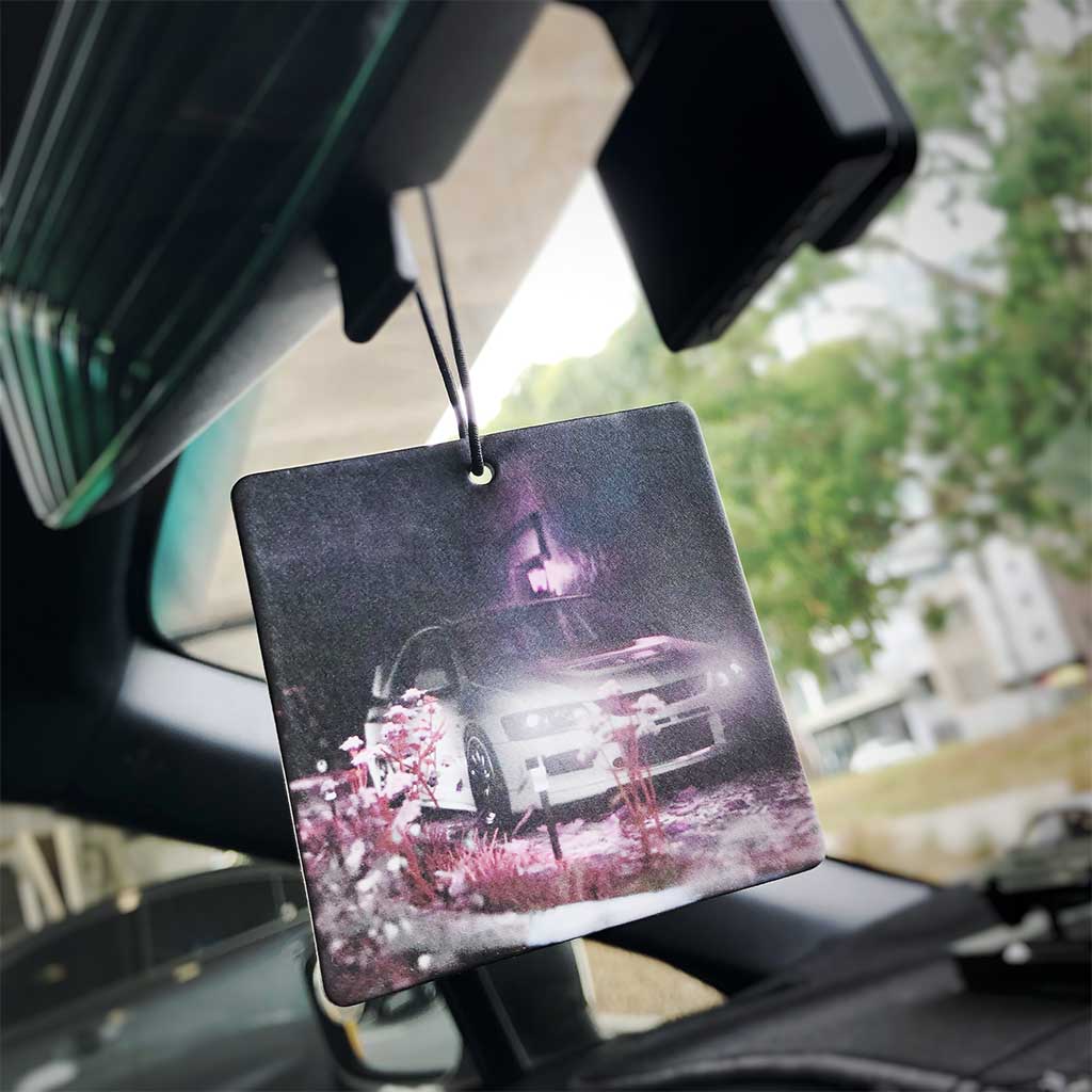 An air freshener with a pattern of an Mitsubishi EVO behind some pink cherry blossoms hung on a car's rearview mirror