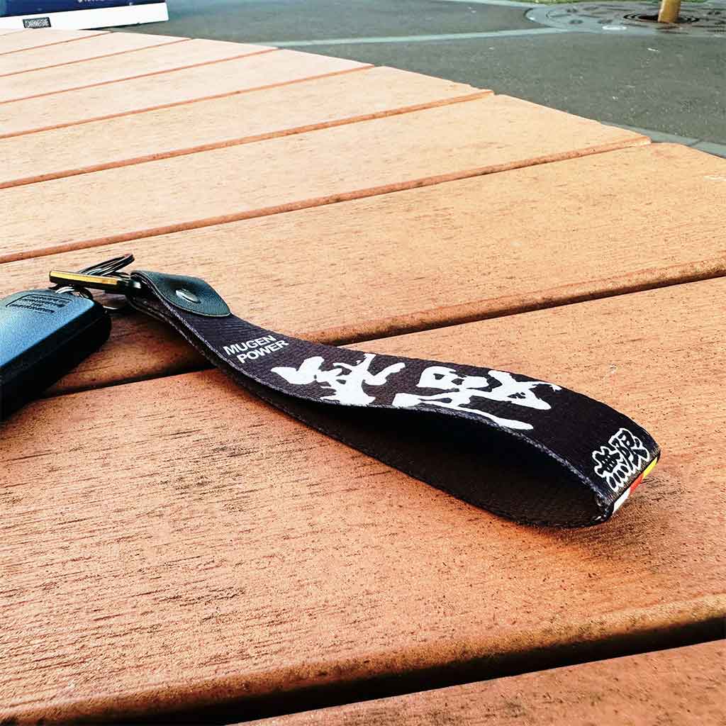 A black lanyard holding a car key placed on a wooden bench