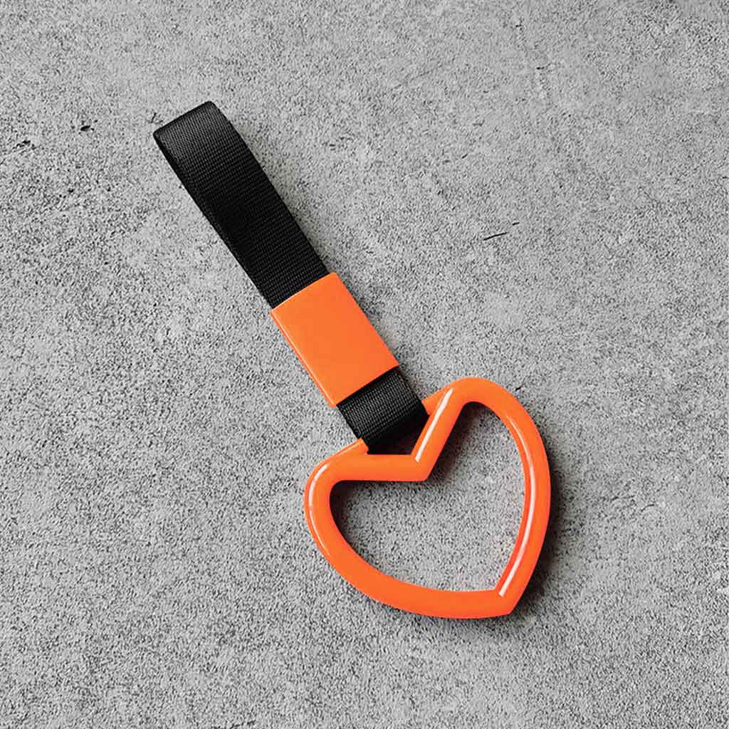 A orange heart tsurikawa with black handle strap flat laid on a concrete floor