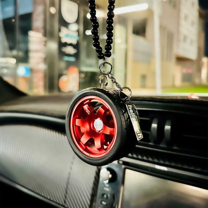 A red TE37 air-freshener hung on a car's rear mirror, with well-lit but blurred street views at the background