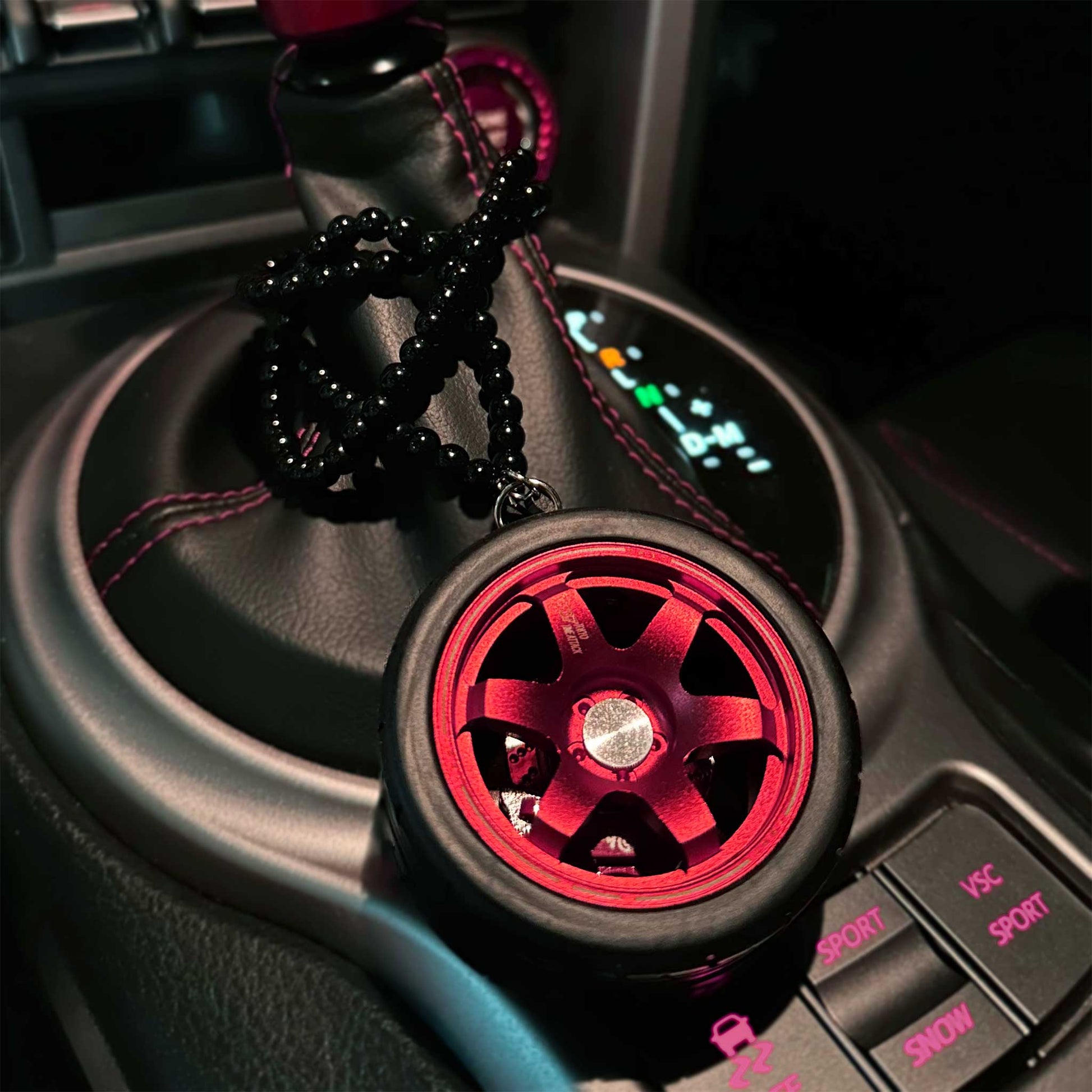 A red TE37 air-freshener is placed on an auto car's console with its beads twining around the car's shift boot