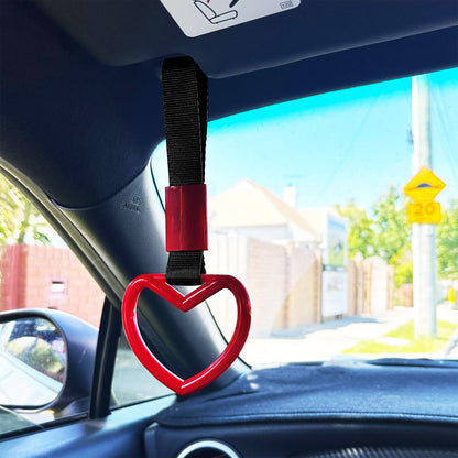 A red heart tsurikawa with black handle strap hung in a Toyota 86 with blue sky and residential houses at the back