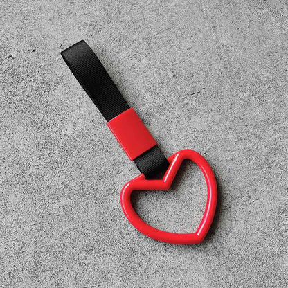 A red heart tsurikawa with black handle strap flat laid on a concrete floor