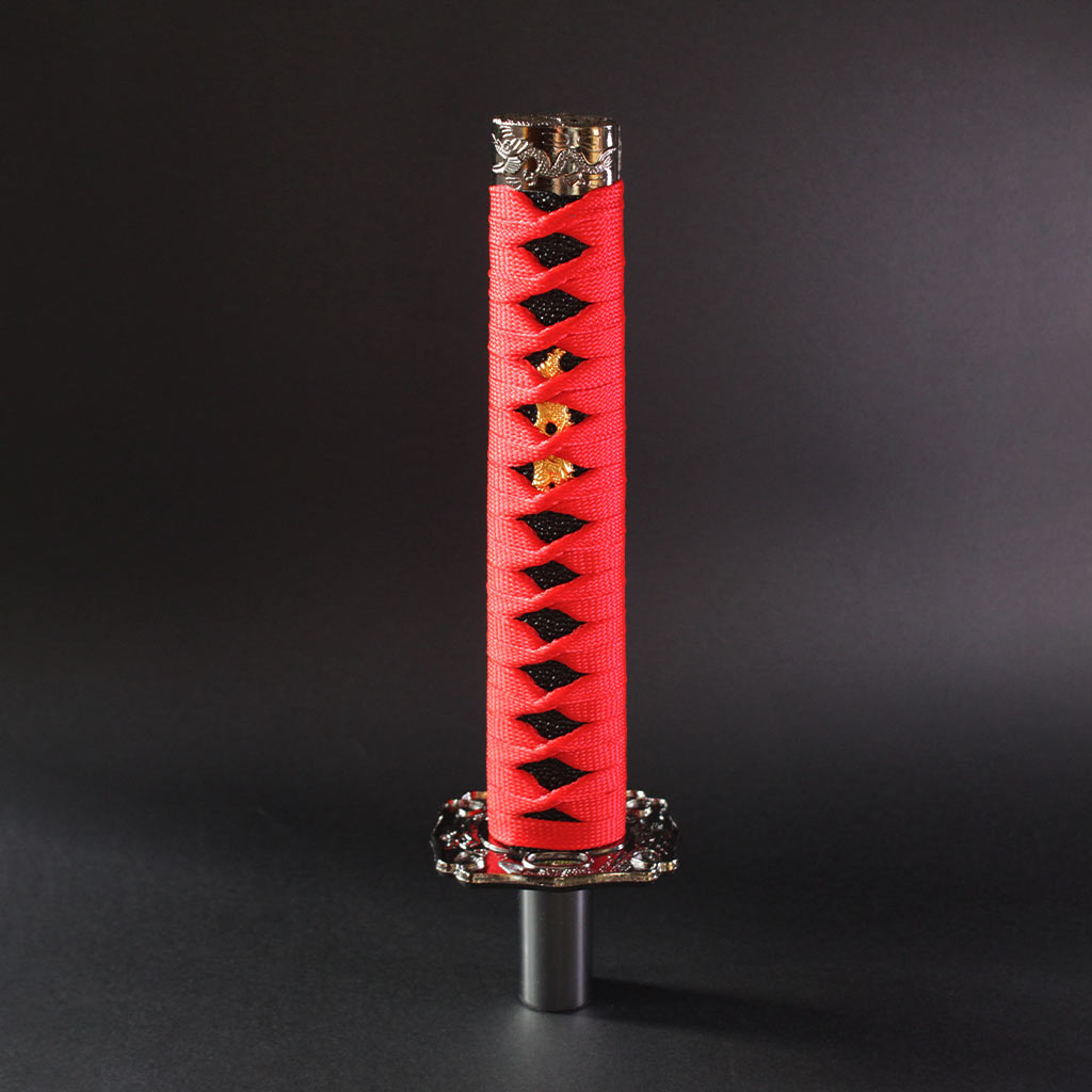 A red and black katana shift knob is standing upright on a dark grey background
