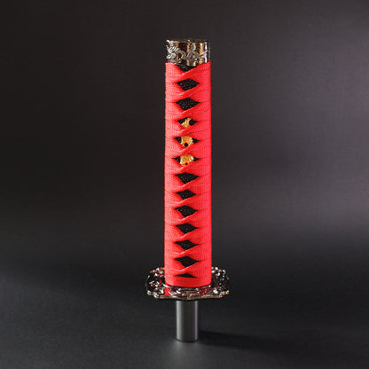 A red and black katana shift knob is standing upright on a dark grey background