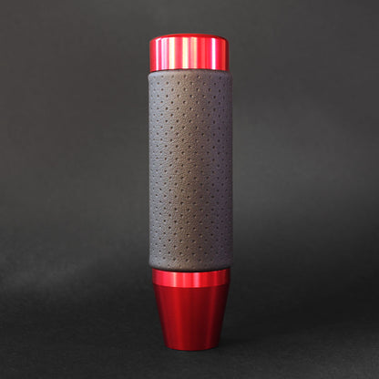 A red leather grip shift knob is standing on a dark grey floor on a dark grey background