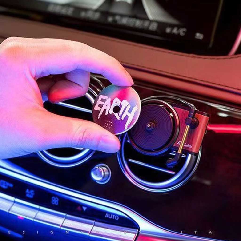 A hand is putting a disc fragrance onto the mini record player air freshener and the air freshener is clipped on a car's air con vents 
