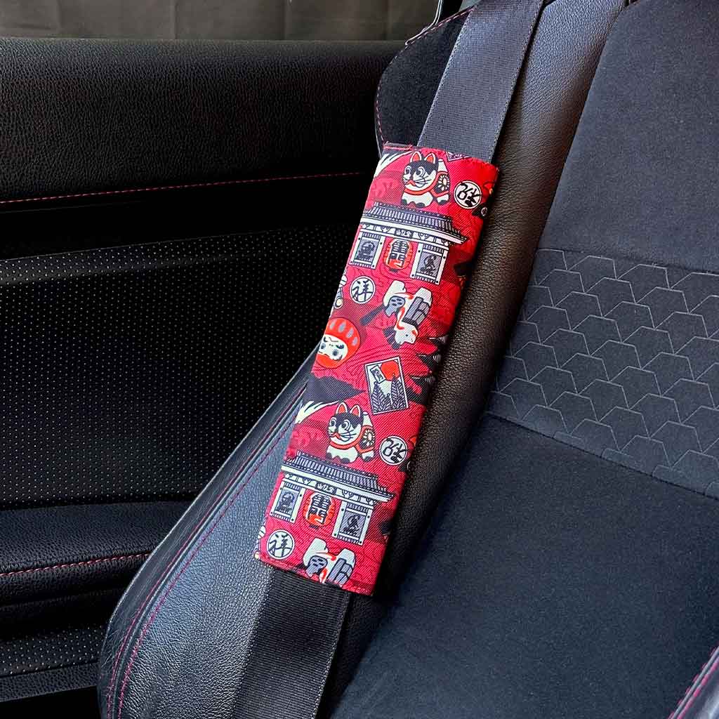 A piece of JDM seat belt cover featuring Japanese elements such as daruma and lucky cat installed in a Toyota 86