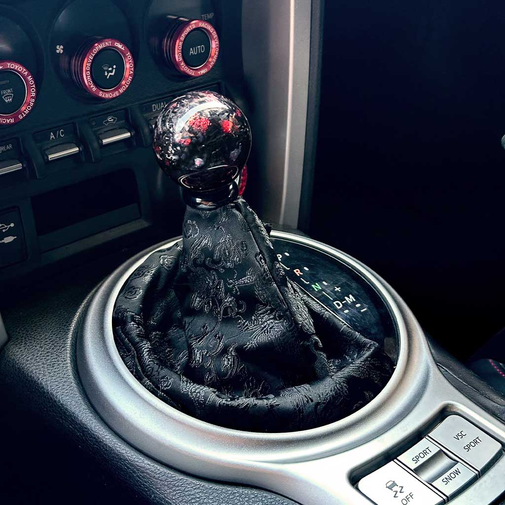 An all-black cool JDM shift boot installed in an automatic Toyota 86, with a red carbon fibre shift knob on top