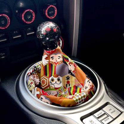 A cute JDM shift boot featuring lucky cat and other Japanese elements installed in an automatic Toyota 86, with a red carbon fibre shift knob on top