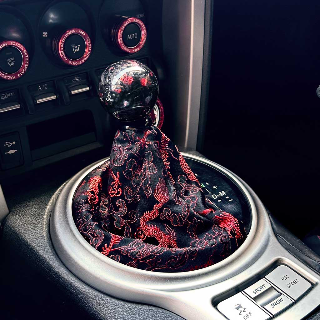 A cool JDM shift boot featuring red Eastern Dragons installed in an automatic Toyota 86, with a red carbon fibre shift knob on top